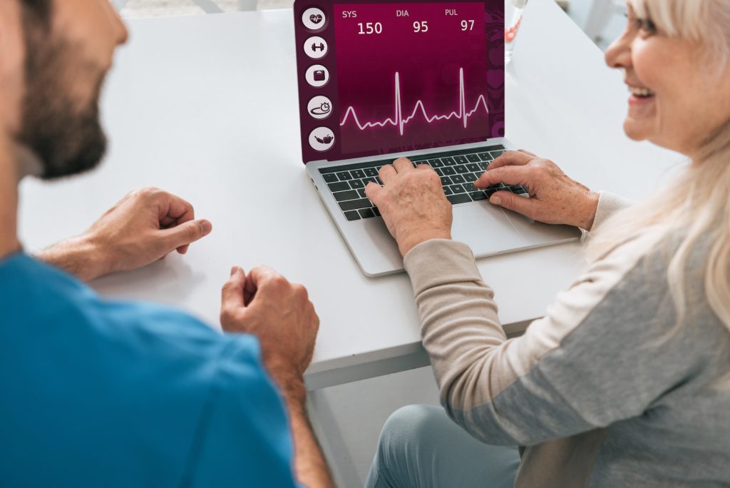 cropped shot of young man and smiling senior woman using laptop with health monitoring application